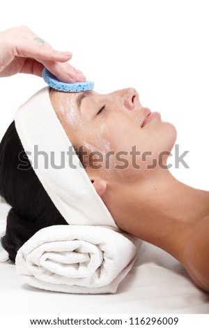 Beautician removing facial mask from woman's face, side view.
