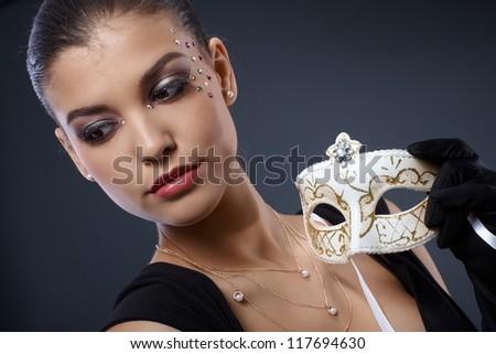 Masquerade elegance of attractive woman wearing glamorous makeup with strasses, holding fancy carnival mask.