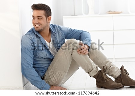 Young man sitting at home on floor, playing peek-a-boo.