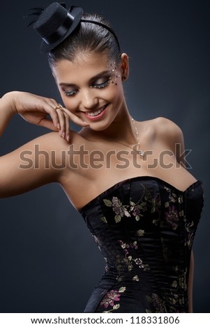 Beautiful woman in extravagant elegant and sexy party dress, wearing little black hat and sparkly makeup with rhinestones.
