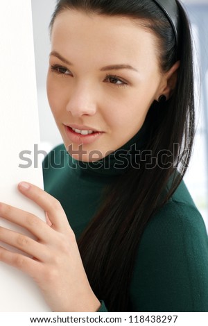 Young attractive girl playing peek-a-boo by wall.