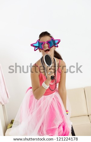 Young girl singing at home in fancy-dress and funny glasses.