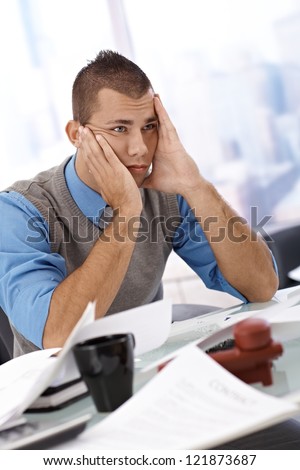 Worried businessman sitting at office desk with face in hands, looking troubled and lost.