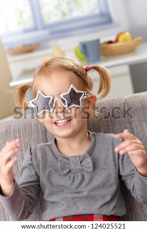 Little girl playing at home, wearing star shaped glasses, smiling.