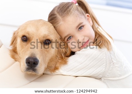 Cute little girl hugging golden retriever with love, looking at camera.