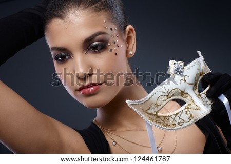 Carnival luxury, portrait of attractive woman in elegant party makeup holding decorated mask.