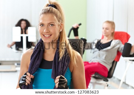 Happy young woman smiling at the gym, towel around neck.