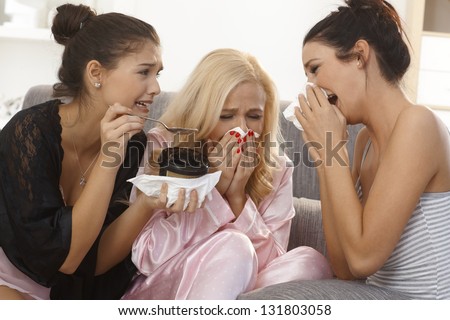 Three female friends crying together at home, wearing pyjamas, blowing nose.