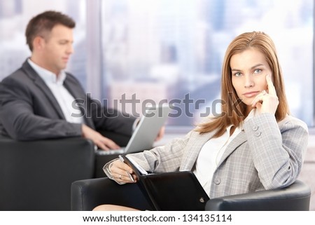 Attractive businesswoman sitting in office lobby in conference break, looking at organizer.