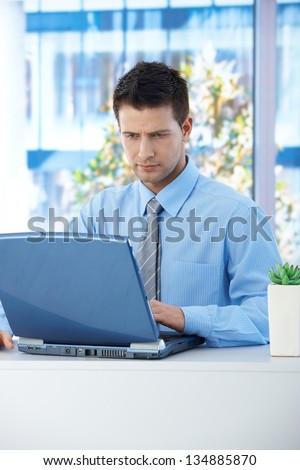 Businessman sitting in office, concentrating on working on laptop computer.