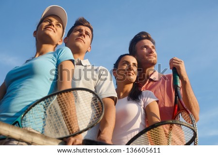 Team of smiling tennis players, photographed from below.