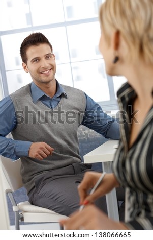 Happy businessman chatting with female colleague at work, smiling.