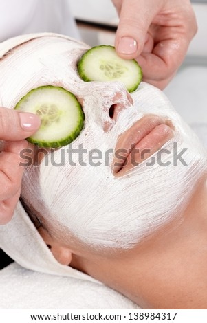 Natural facial treatment, young woman laying with facial mask and cucumber on eyes.