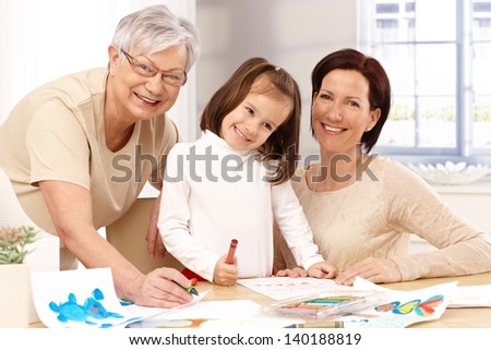 Happy mother, granny and little daughter playing together, drawing at table.
