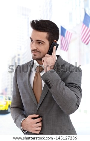 Young businessman on the phone walking outdoors, american flags in background