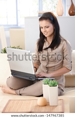 Young woman working on computer at home, smiling.