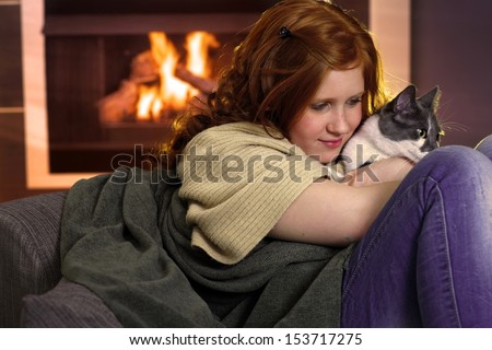 Red hair teenager girl fondling cat at home sitting by fireplace.