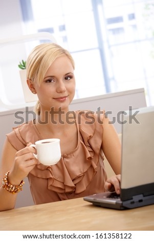 Portrait of young attractive blonde office worker woman on coffee break, using computer.
