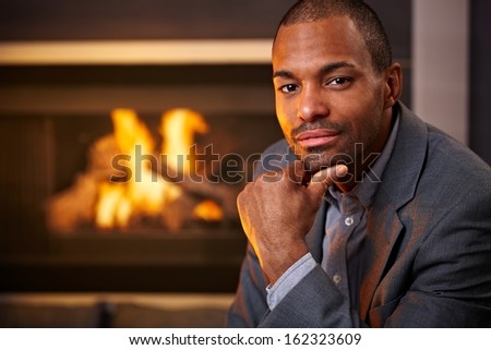 Portrait of handsome black man sitting at home by fireplace.