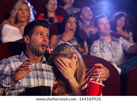 Young couple watching horror movie in cinema, girl turning her head away with fear.