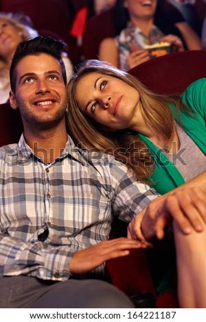Romantic couple watching movie in cinema, smiling.