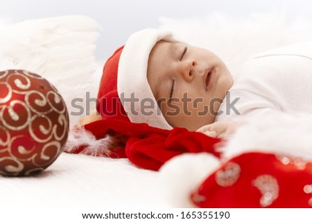 Closeup portrait of newborn baby sleeping in santa hat with christmas ornament.