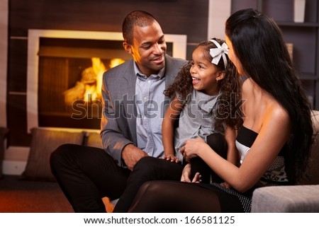 Happy ethnic family of three in living room by fireplace.