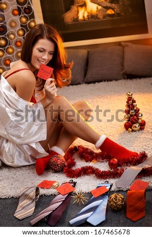 Sexy woman in silk gown and christmas socks arranging christmas gifts, tie with name tag for men.