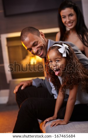 Beautiful diverse family having fun at home, little daughter sticking tongue, smiling.