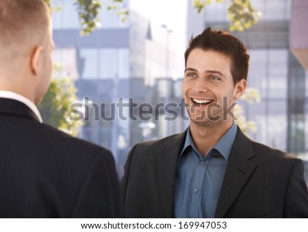 Laughing coworkers standing outside of business office, talking.
