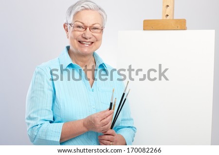Happy old lady as hobby painter with canvas and paintbrush.