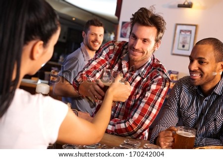 Happy young man getting a glass of beer from female bartender at counter, smiling.
