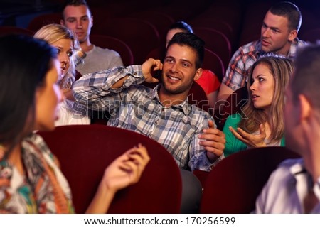 Confident young man talking on mobilephone in cinema, spectators looking angry.