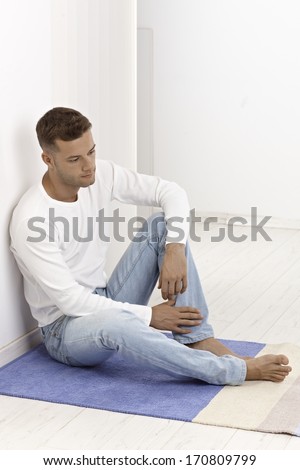 Young man sitting on floor at home, looking sad.