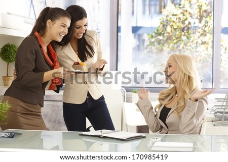 Young female office workers celebrating ones birthday, bringing cake with candle.