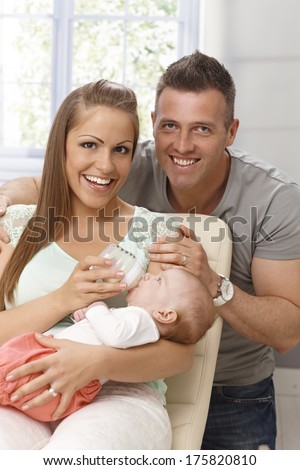 Portrait of happy smiling couple holding newborn baby, feeding her from bottle.