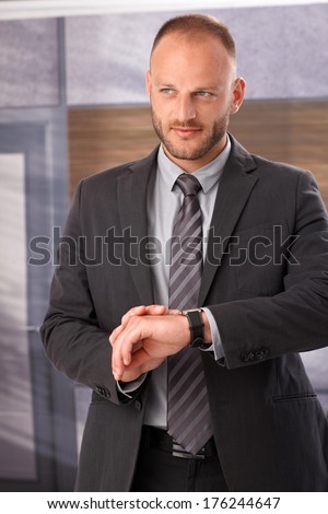 Businessman checking time on wristwatch, waiting, standing.