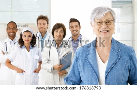 Happy senior woman with medical team in background.