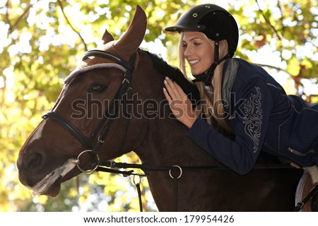 Closeup photo of attractive female rider leaning over horse, smiling happy.