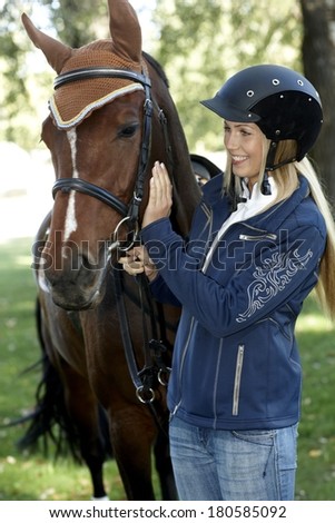 Female rider in equestrian helmet caressing horse, smiling.