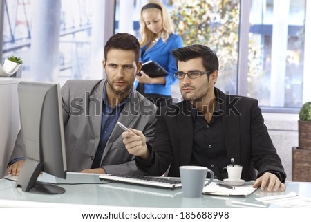 Businessmen working together, sitting at desk, using computer.
