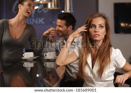 Unhappy young woman sitting in bar, boyfriend flirting with waitress at background.