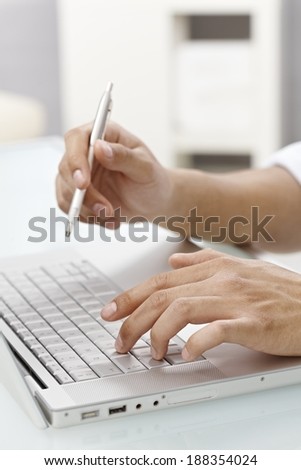 Closeup photo of hand typing on laptop keyboard, right hand holding pen.