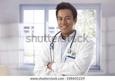 Portrait of happy young male doctor standing arms crossed, looking at camera.