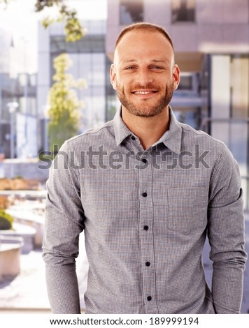 Outdoor photo of happy young man smiling, looking at camera.