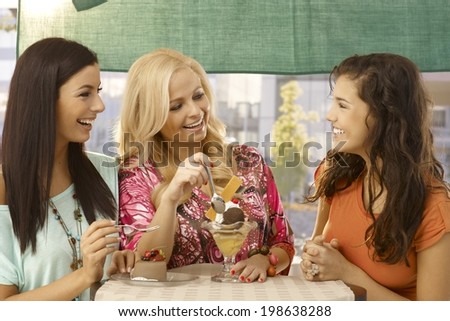 Female friends having sweets at outdoor cafe, chatting, smiling happy.