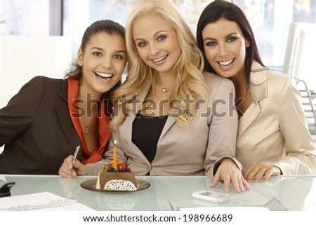 Closeup portrait of three happy businesswomen celebrating ones birthday at workplace with chocolate cake and candle.