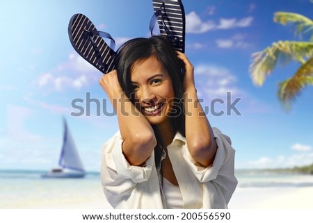 Beautiful woman having fun on the beach at summertime. Holding flip flop, smiling happy.