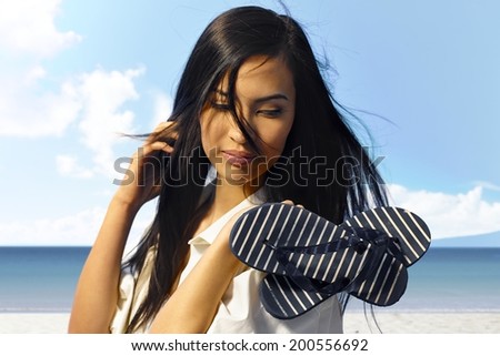 Summer portrait of beautiful young woman on the coast. Holding flip flop in hands.