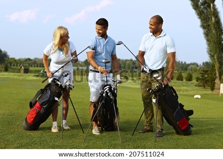 Happy partners standing on golf course, choosing golf club from golfing kit, starting game.